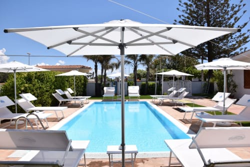Piscina del resort con lettini e ombrelloni bianchi presso Villa Blanche Holidays a Marsala, Italia