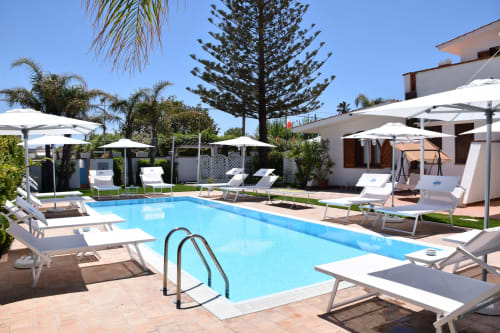 Area piscina Villa Blanche Holidays a Marsala con lettini, ombrelloni e palme sotto cielo sereno