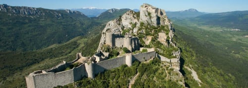Château médiéval perché sur un pic rocheux, entouré de montagnes boisées près de Thuir, France