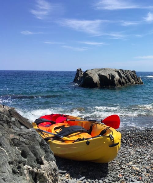 Kayaks jaunes et rouges sur plage rocheuse près de Thuir, mer turquoise et formations rocheuses sous ciel bleu