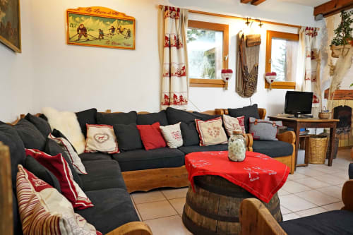 Salon douillet du refuge alpin L'étape Du Fanfoué à Chamrousse avec canapé noir, accents rouges et poutres apparentes.