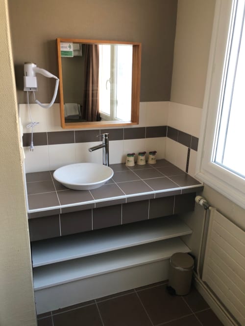 Modern bathroom vanity with round white sink, wooden mirror, dark and white tile at Hôtel Maison Richet Les Sables-d'Olonne