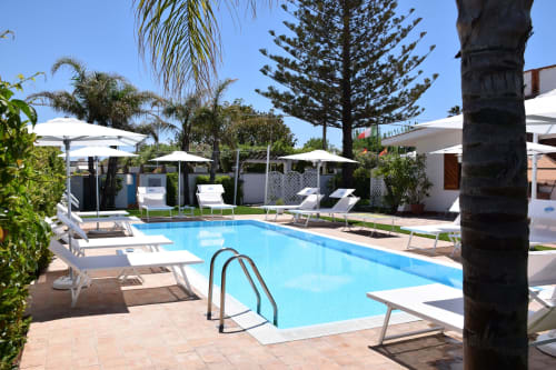 Area piscina di Villa Blanche Holidays a Marsala con lettini, ombrelloni e palme sotto cielo sereno