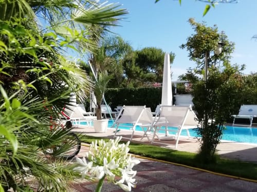 Area lounge soleggiata a bordo piscina a Villa Blanche Holidays a Marsala con ombrelloni bianchi, lettini e lussureggianti giardini tropicali