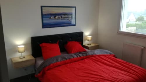 Chambre lumineuse à la Résidence des dunes avec literie rouge, tête de lit noire et œuvres côtières à Landéda