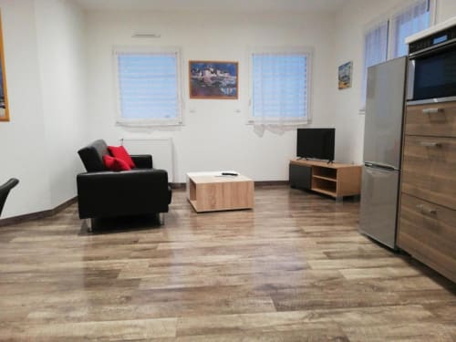 Espace de vie ouvert et moderne à la Résidence des dunes, Landéda avec canapé noir, parquet, cuisine et télévision.