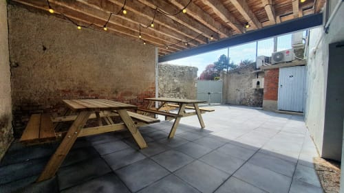 Covered terrace with wooden picnic tables at Locacharme cottage, Blois, overlooking river with stone walls and string lights