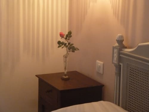 Elegant hotel room detail at Château De Clusors showing wooden desk with fresh rose in vase, radiator, and warm curtained