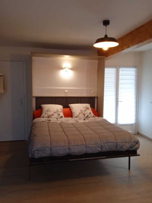 Chambre moderne aux Clématites en Cotentin avec lit queen-size, accents rouges, luminaire suspendu et portes vitrées vue sur la rivière