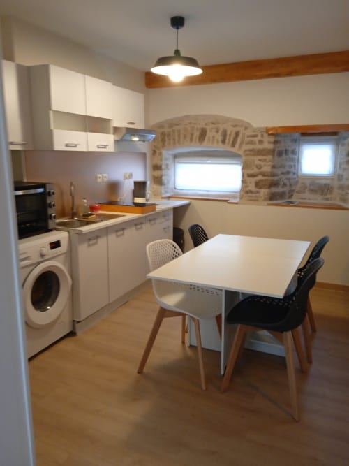 Cuisine-salle à manger contemporaine avec armoires blanches, table de repas, machine à laver et arche en pierre à Varette Patricia Les