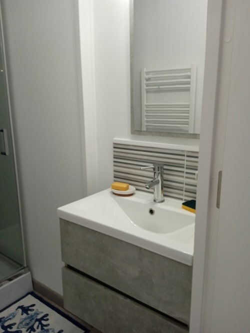 Lavabo de salle de bain moderne avec plan de travail blanc, robinet chromé et carrelage rayé à l'hôtel Varette Patricia