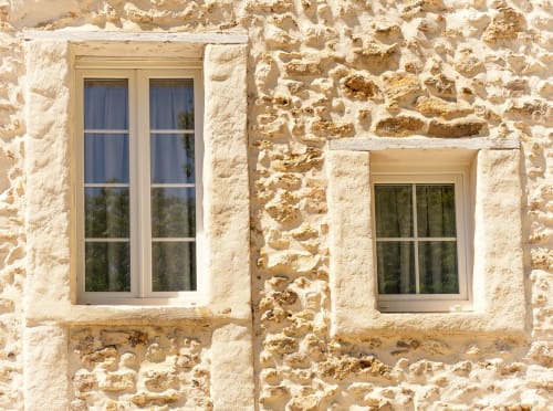 Rustic stone facade of Le Petit Château B&B in Baye, France with cream windows