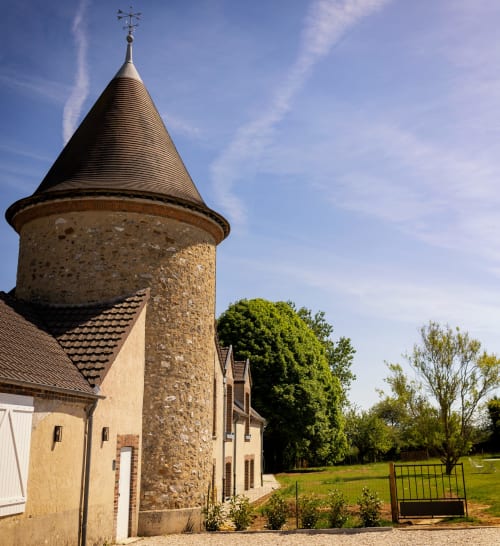 Historic stone tower with conical roof at Le Petit Château bed and breakfast in Baye, France, surrounded by green fields