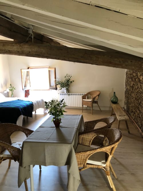 Habitación abuhardillada luminosa en Casa Tapiolas de Molló con sillas de mimbre, mesa de comedor y vistas a la montaña desde la ventana abierta