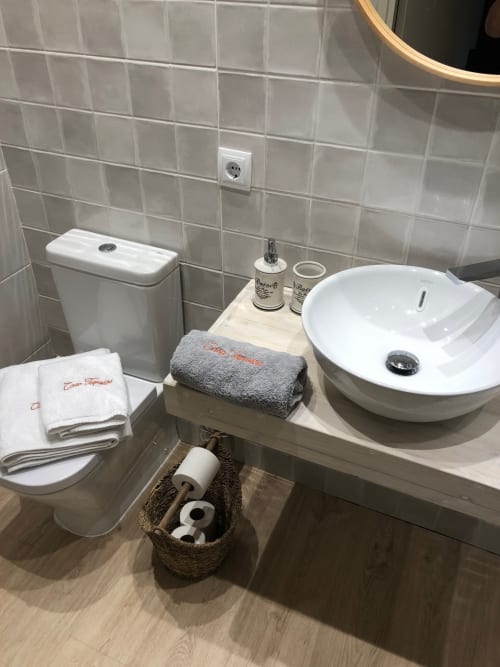 Baño moderno en Casa Tapiolas con lavabo blanco de cerámica, inodoro, azulejos grises, toallas y artículos de aseo en Molló, Girona