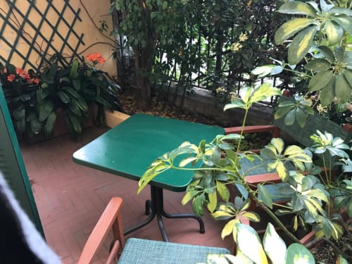 Gartenterrasse mit grünem Tisch im Hotel Beau Rivage in Alassio, umgeben von üppigen Pflanzen und Blüten