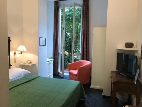 Hotelzimmer Beau Rivage mit grünem Bett, Flachbildfernseher, rotem Sessel und Glastüren mit Gartenblick in Alassio