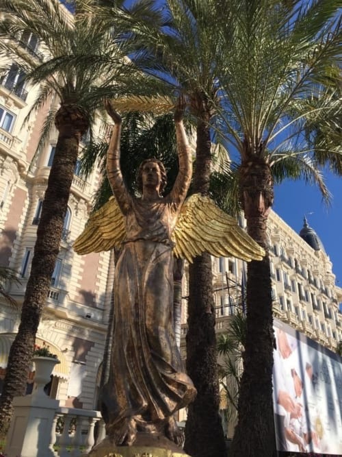 Golden-winged angel statue surrounded by palm trees in Cannes, France
