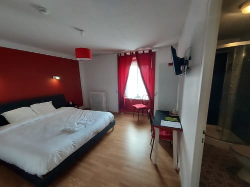 Chambre moderne au B&B Le Comtois en Saône avec mur d'accent rouge, literie blanche et rideaux cramoisis