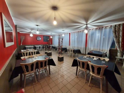 Salle à manger Le Comtois aux murs rouges, chaises en bois et luminaires suspendus à Saône, France