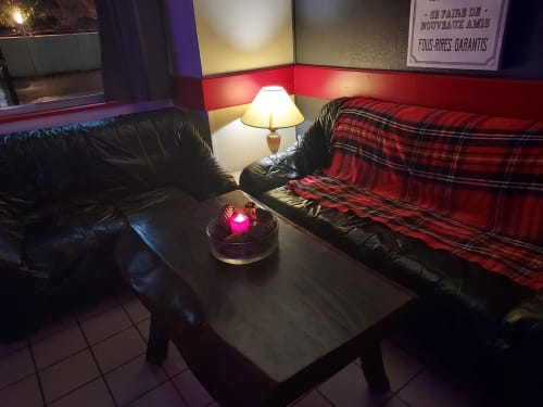 Salon confortable au Gîte Le Comtois à Saône avec canapés en cuir noir, plaid écossais rouge, lampe et éclairage tamisé