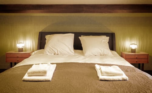 Luxe slaapkamer in Le Petit Château met crèmekleurig beddengoed, donker hoofdeinde, houten nachtkastjes en warm licht bij Souverain