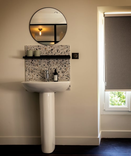 Modern bathroom at Le Petit Château B&B in Baye with pedestal sink, terrazzo backsplash, and circular mirror with garden view