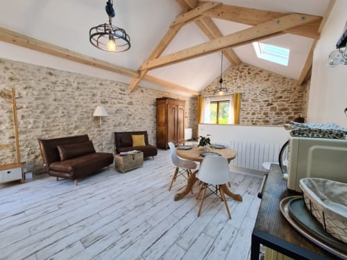 The Cowshed cottage at Aux Prés Du Berry features exposed beams, stone walls, dining area, and brown leather seating in