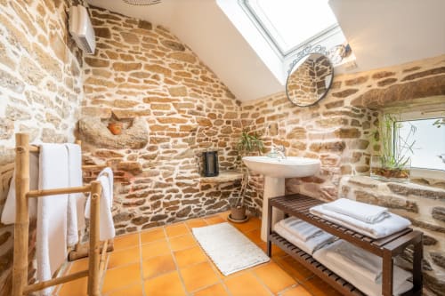Rustic stone bathroom at Espace Ker Gana in Plourin with terracotta tiles, pedestal sink, and skylight window