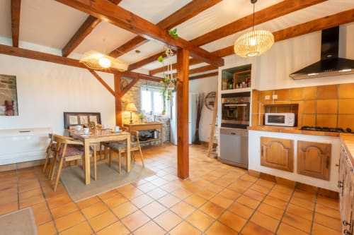 Spacious modern kitchen with wooden beams at Maison Berce in Plourin, featuring dining area and terracotta floors