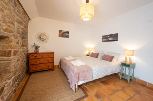 Spacious bedroom at Espace Ker Gana in Plourin with twin beds, terracotta tile floor, wooden dresser, and exposed stone wall