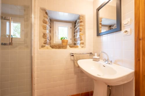 Modern bathroom at Espace Ker Gana in Plourin with white tiles, pedestal sink, mirror, and glass shower enclosure with rustic