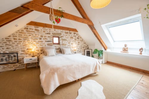 Rustic bedroom at Espace Ker Gana B&B in Plourin with exposed stone walls, wooden beams, and skylights.