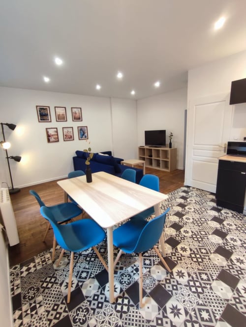 Appartement moderne à Montargis avec coin repas, chaises bleues, séjour, téléviseur et carrelage géométrique