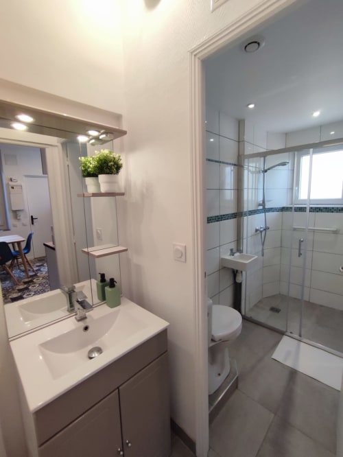 Salle de bain moderne à Lesdoucesnuits45 à Montargis avec vanité blanche, miroir, douche vitrée et toilettes