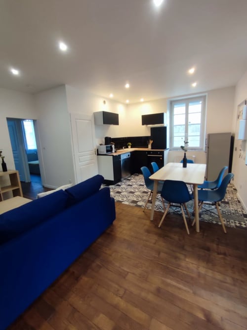 Appartement moderne Lesdoucesnuits45 à Montargis avec canapé bleu, table à manger, cuisine noire et télévisions écran plat