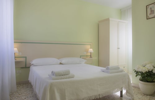 Camera luminosa verde salvia a Il Linchetto B&B a Lucca con letto bianco, asciugamani, armadio e fiori in vaso