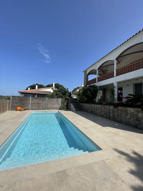 Das rechteckige Schwimmbecken des Ty Pals B&B in Pals besticht mit türkisblauem Wasser, umgeben von beigefarbiger Terrasse und moderner weißer Architektur