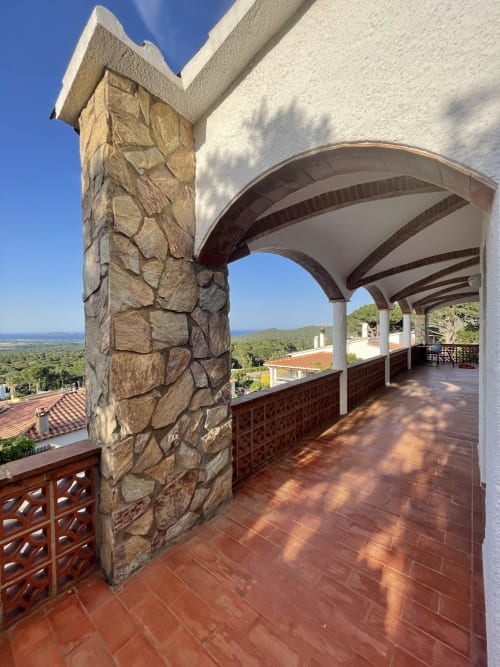 Covered terrace with stone column at Ty Pals villa in Pals, overlooking Mediterranean sea and countryside
