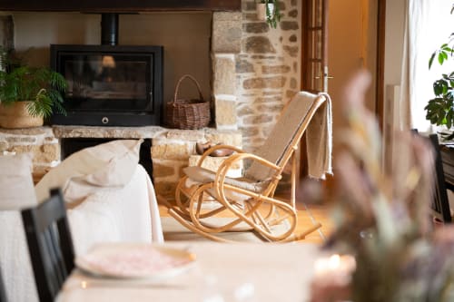 Salon douillet de la maison d'hôtes Espace Ker Gana avec cheminée en pierre, rocking-chair en bois et charme rustique à Plourin