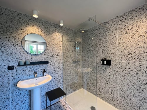 Salle de bain moderne du Petit Château avec murs en terrazzo, miroir rond, lavabo sur piédestal et douche à l'italienne