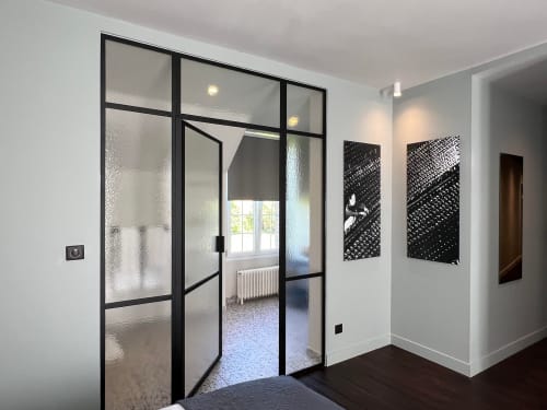 Chambre Réhoboam du Petit Château avec cloison vitrée à cadre noir, murs blancs et vue sur le jardin