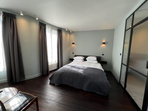 Chambre moderne au Petit Château à Baye avec parquet foncé, lit queen-size, murs gris et fenêtres avec vue sur le jardin