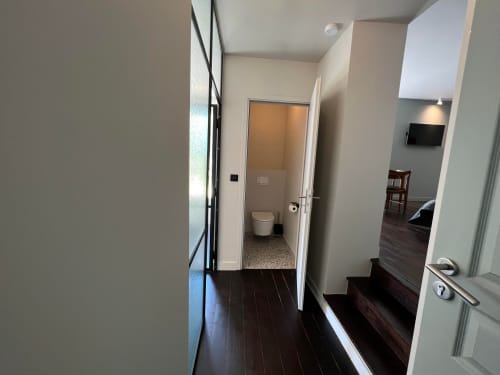Modern hallway with dark wood flooring and white walls leading to bathroom at Le Petit Château in Baye, France