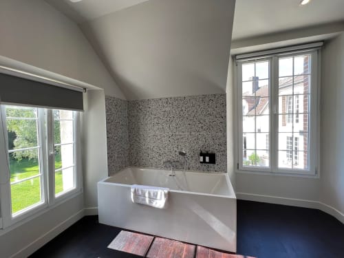 Modern bathroom in Le Petit Château with white soaking tub, speckled tile accent wall, and garden views through double
