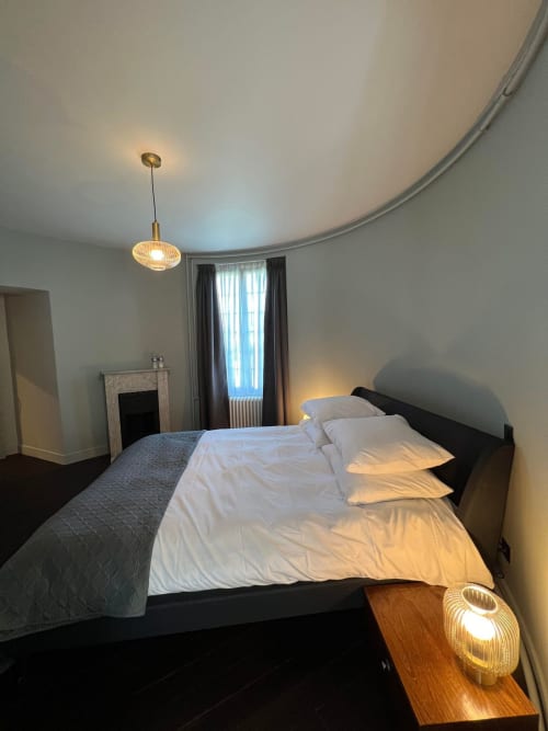 Moderne slaapkamer in de toren van Le Petit Château met zwart bed, witte lakens, hangende verlichting en uitzicht op de tuin