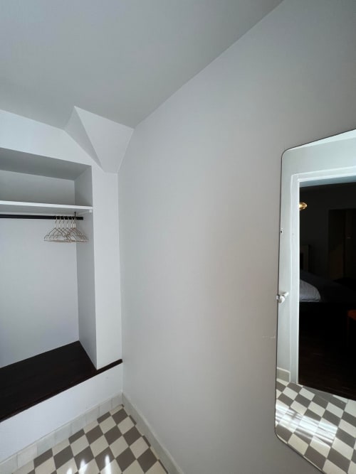 Moderne inloopkast met witte muren, zwarte plinten, geruit vloer en kledingroede met hangers bij boutique Le Petit Château