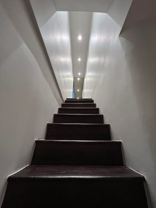 Modern trappenhuisbij Le Petit Château met donkere treden en witte wanden, opgaand met eigentijdse verlichting