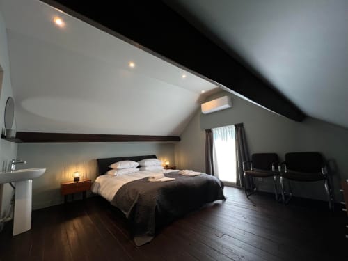 Moderne zolderslaapkamer in Le Petit Château met queensize bed, wit plafond, donkere balken en uitzicht op de tuin