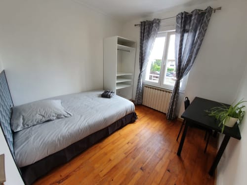Chambre lumineuse du gîte NancyRoom avec parquet, lit, armoire, bureau et vue sur la ville à Vandoeuvre-lès-Nancy